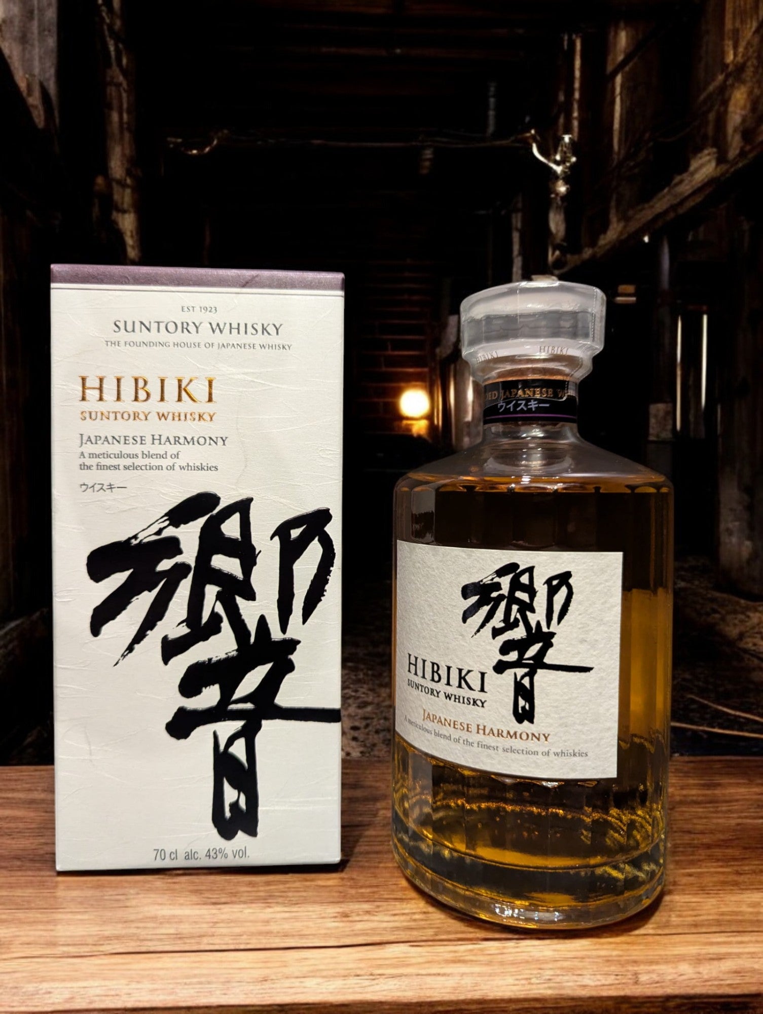 Flasche Suntory Hibiki Harmony Whisky vor einem dunkelgrauen Hintergrund, wobei das edle Design der Flasche mit ihrer facettenreichen Glasstruktur und das elegante Etikett mit goldener Schrift durch den Kontrast hervorgehoben werden und der goldene Farbton des Whiskys sanft durchscheint.