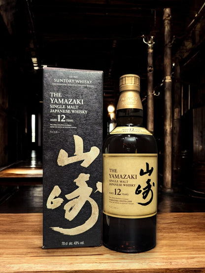 Detailaufnahme der Suntory Yamazaki Whiskyflasche, umgeben von Eichenfässern im Lagerhaus. Das warme Licht unterstreicht die goldbraune Farbe des edlen Single Malt Whiskys. Der Name Yamazaki prangt stolz auf dem Etikett, was auf die traditionsreiche Whiskybrennerei in Japan hinweist. Die Szene vermittelt eine Atmosphäre von Qualität und Handwerkskunst, die in der Herstellung dieses renommierten Getränks steckt.