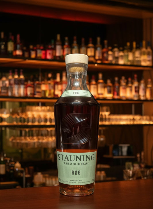 Whiskyquartier Stauning RØG Smoked Double Malt Danish Whisky in a tall glass bottle with a light wood stopper. Amber liquid with golden hues.