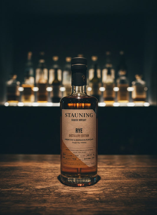 Whiskyquartier Stauning Rye Distillery Edition in Virgin Oak & Barbados Rum Cask, 0,35L, 53,5% Vol. auf Sand mit Strandhafer und Meer im Hintergrund.